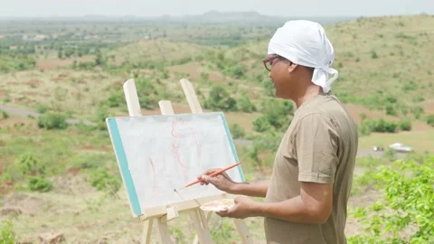 Artist painting or drawing on canvas board by seeing mountians and nature at top Stock Footage