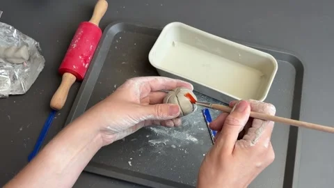 Artist scoring a small clay pumpkin with a wooden modeling tool on a craft tray Stock Footage 345719250