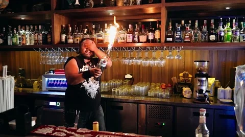 Artistic bartender with piercings + dreadlocks juggling bottle torch and shaker Stock Footage 65398308