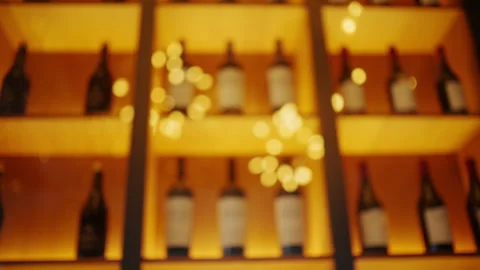 Artistic blurred shot of wine bottles displayed on illuminated shelves with warm Stock Footage 335223392