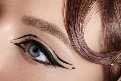 Artistic eye makeup featuring bold black winged eyeliner and small gold dots Stock Photos