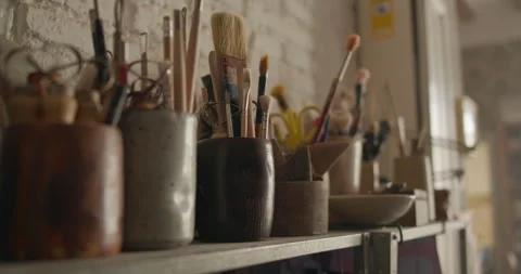 Artists hand selecting a paintbrush from a shelf filled with tools in a ceramic Stock Footage 302554353
