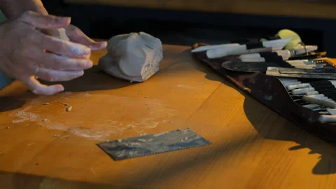 Artist's hands shaping and rolling raw clay on a wooden workbench 스톡 동영상 344650375