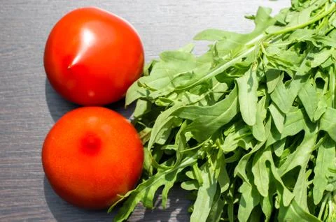 Arugula and two red tomatoes on a brown wooden background Stock Photos