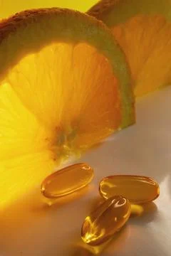Ascorbic acid softgels in foreground.Oranges in background Stock Photos
