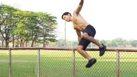 Asia man Slow Motion Jumping Over Hurdle  Steel Mesh Fence on Foot Ball Field. Stock Footage 107092079