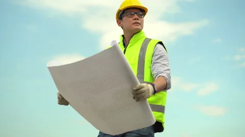Asian architect checking construction site with blueprint outdoors on blue sk Stock Footage 146444864