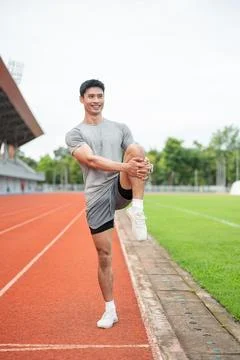 Asian athlete man smiling while doing single leg knee hug stretch on track .. Stock Photos