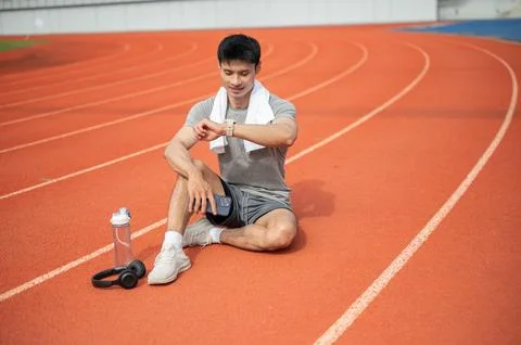 Asian athletic man checking time or reviewing smartwatch while recovering o.. Stock Photos
