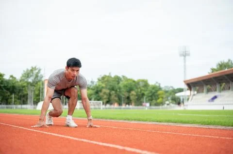 Asian athletic man leaning forward to sprint in starting position during tr.. Stock Photos