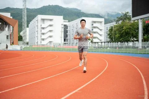Asian athletic man smiling while jogging on red running track in sports stadi Fotos Stock
