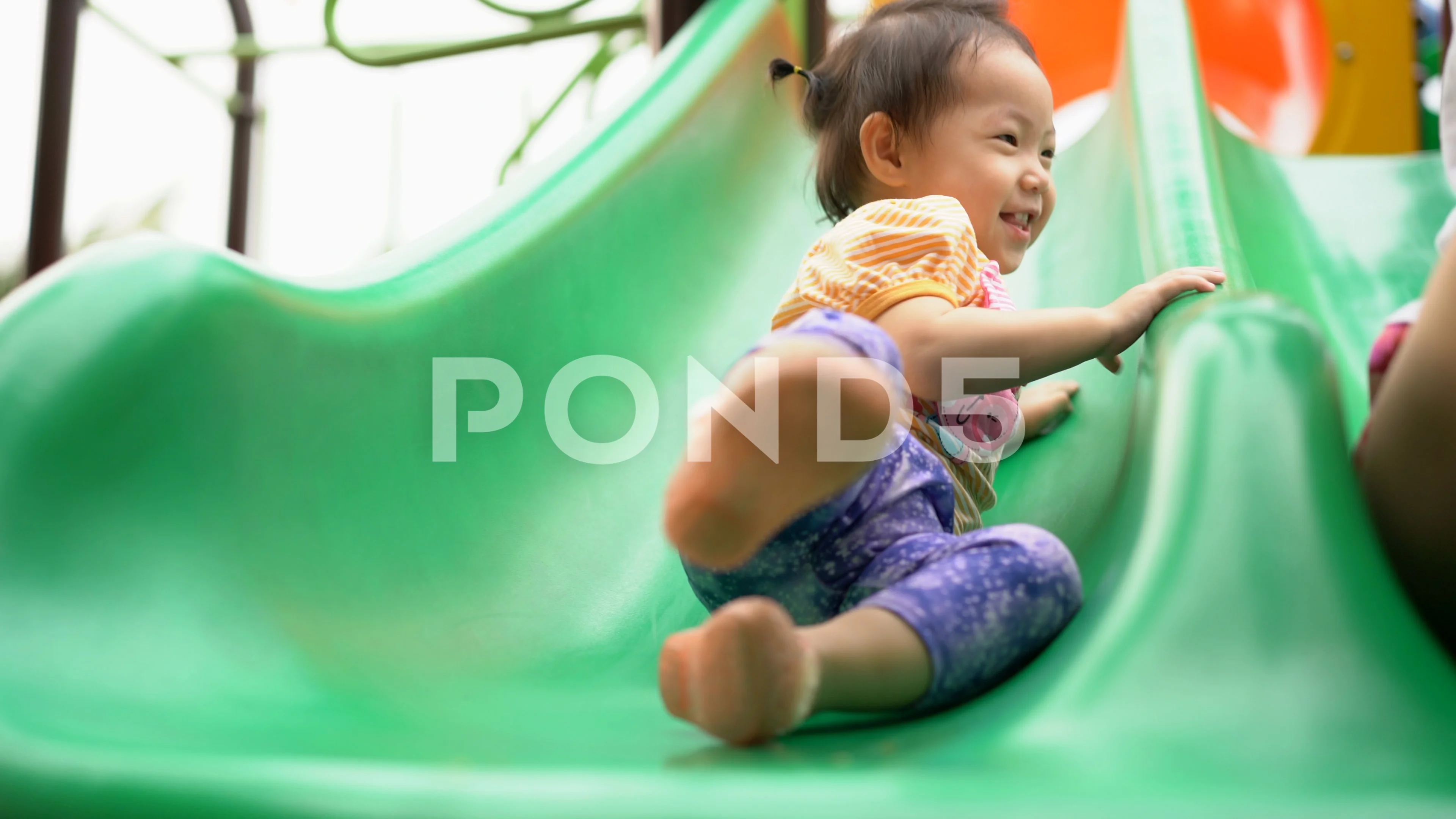 A Little Girl Sliding Down A Green Slide At The Playground. by
