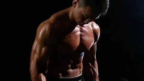 Asian bodybuilder training biceps with a barbell. Black smoke background. Slow Stock Footage 75076050