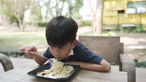 Asian boy about 5 years old with face mask under the chin eating spaghetti Vídeos de archivo 152290532