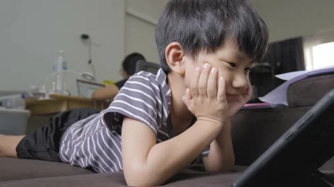 Asian boy addicted watching tablet while his mother working. Stock Footage 220244723