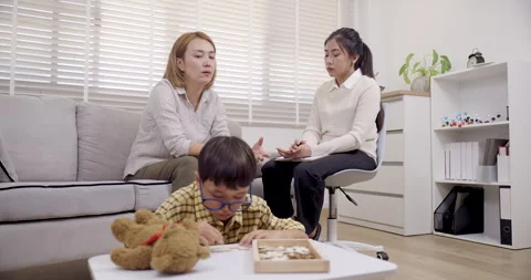 Asian boy with adhd sits on floor playing puzzle near sofa while single mother Stock Footage 313741184