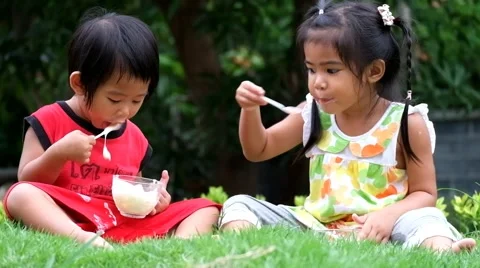 Asian boy and girl are eating delicious yogurt at the park Stock Footage