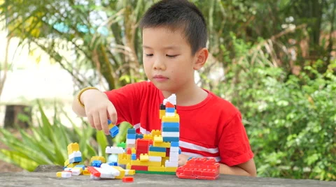 Asian boy build plastic block on wooden table in park Stock Footage 63042444