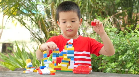 Asian boy build plastic block on wooden table in park Stock Footage 63047467