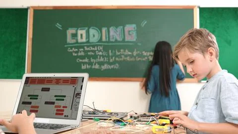 Asian boy coding program while friend fixing electric board at class. Pedagogy. Stock Photos