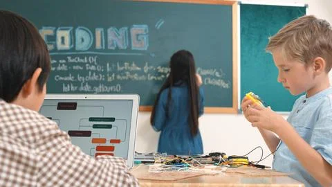Asian boy coding program while friend fixing electric board at class. Pedagogy. Stock Photos