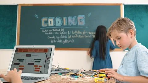 Asian boy coding program while friend fixing electric board at class. Pedagogy. Stock Photos