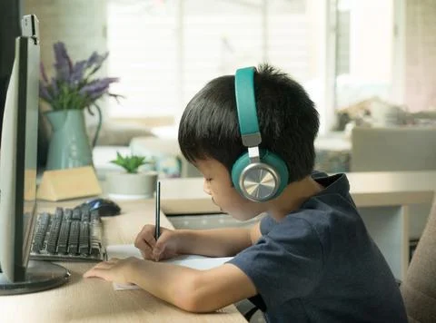 Asian boy concentrates on e-learning during Covid-19 pandemic and social dist Stock Photos