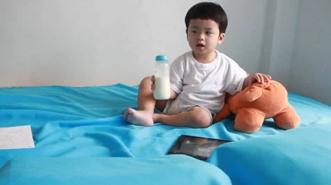 Asian boy drinking milk from bottle on the bed and see tablet. 스톡 동영상 55425147