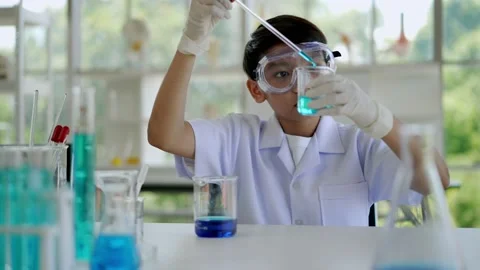 Asian boy drop dark blue liquid into beaker in laboratory Stock Footage 201361355