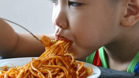 Asian boy with fork in hands eats pasta, close-up Stockbeeldmateriaal 74653628