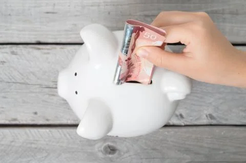 Asian boy hand inserting a fifty dollars bank note into white piggy bank  aga Stock Photos