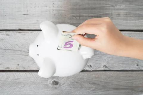 Asian boy hand inserting a five dollars bank note into white piggy bank  agai Stock Photos