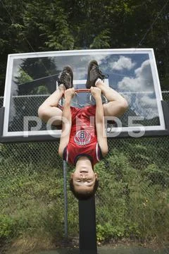 Asian Boy Hanging Upside Down On Basketball Hoop