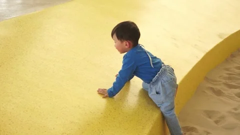 An Asian boy is learning to crawl on a sloped surface in a playground. Stock Footage 301059342