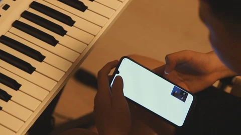 Asian boy learning piano by himself by looking up notes on his phone Stock Footage 107936394