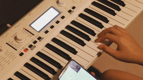 Asian boy learning piano by himself by looking up notes on his phone Stock Footage 107936730