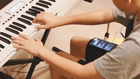 Asian boy learning piano by himself by looking up notes on his phone Video stock 107936813