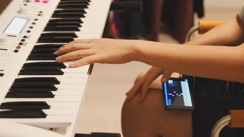 Asian boy learning piano by himself by following a video on his smartphone Stock Footage 107936856