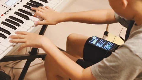 Asian boy learning piano by himself by looking up notes on his phone Stock Footage 107936914