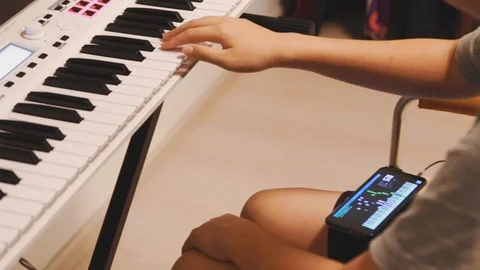 Asian boy learning piano by himself by following a video on his smartphone Stock Footage 107936918