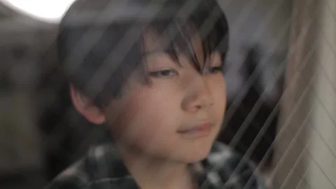 Asian boy looks outside through the window. Thoughtful face. Stock Footage 224291395