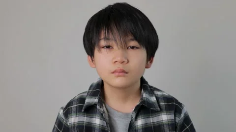 Asian boy opens his eyes and stares the camera. Unsatisfied. Dolly out. Stock Footage 221380220