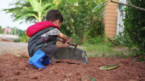 Asian boy playing and digging soil using steel hoe Stock Footage 95792356