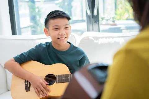 Asian boy playing guitar with father in the living room for teaching him son  Stock Photos