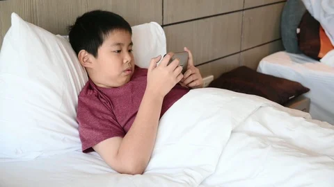 Asian boy playing smartphone on bed, Stock Footage 124114639