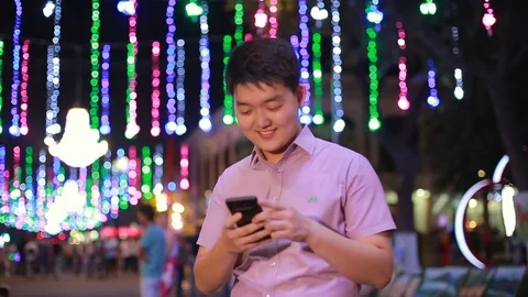 Asian boy prints a message at night in the Park where a lot of lights. Gesturing Stock Footage 93259343