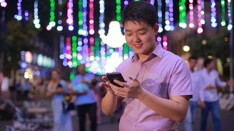Asian boy prints a message at night in the Park where a lot of lights. Gesturing Stock Footage 93260086