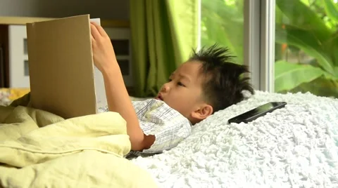 Asian boy reading book on the bed Stock Footage 53356461