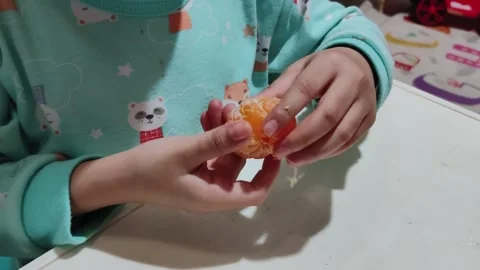 An Asian boy sits at a table peeling tangerines. Stock Footage 296928664