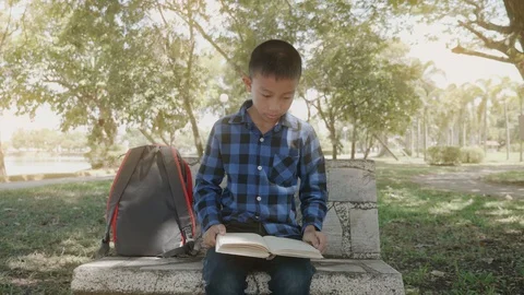 Asian boy sitting on bench and reading book at public park. Stock Footage 118870751